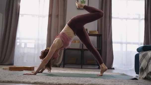 Hemma fitness av vuxen smal kvinna i vardagsrummet, öva hatha yoga, utför asanas, sportig dam tränar i lägenhet — Stockvideo