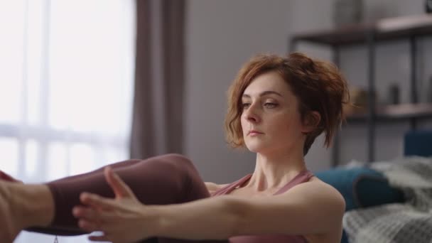 Портрет взрослой женщины-практикующей йоги, тренирующейся в одиночестве в своей квартире, выполняющей позу для баланса тела, сидящей на полу — стоковое видео