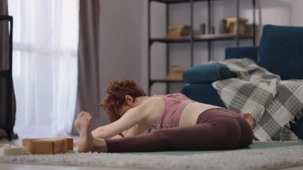 Mujer flexible deportiva está haciendo split y estiramiento en casa, sentado en el suelo en la sala de estar, ejercicios de yoga y gimnasia — Vídeos de Stock