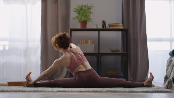 집에서 체조를 하고 있는 젊고 날씬 한 여자는 거실에서 다리 근육을 펴고 뒷모습을 훈련하고 있다 — 비디오