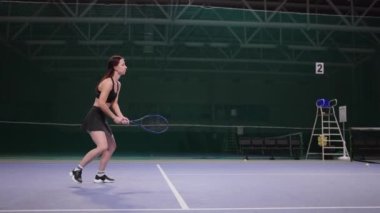 Kadın sporcuların tenis maçı, sportif bayan raketle topa vuruyor, boş iç sahada ilerliyor.