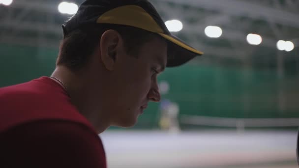 Close-up retrato de tenista masculino na quadra interior antes do jogo importante, o homem está sentado no banco e pensando sobre o jogo — Vídeo de Stock