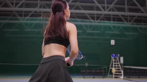 Νεαρή γυναίκα τενίστρια παίζει σε εσωτερικό γήπεδο, εντυπωσιακή μπάλα από ρακέτα τένις, τρέχει πάνω από την περιοχή — Αρχείο Βίντεο