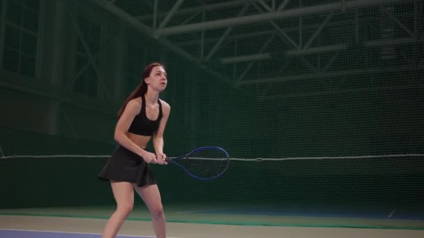 Mladá žena hraje tenis na vnitřním hřišti, odpaluje míček raketou, zpomaluje hru — Stock video