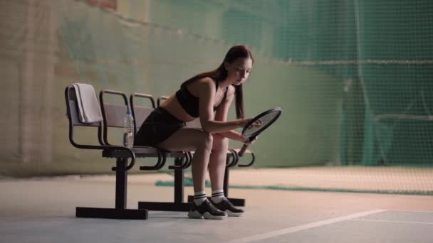 Sportlerin trägt Sportbekleidung sitzt nach Spiel oder Training auf Bank auf Tennisplatz, sportliche Person — Stockvideo