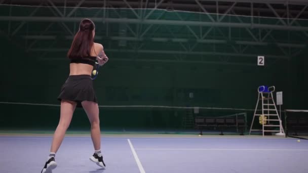 Молодая женщина играет в теннис на крытом корте, ударяя мяч теннисной ракеткой, пробегая по территории, замедленное движение — стоковое видео