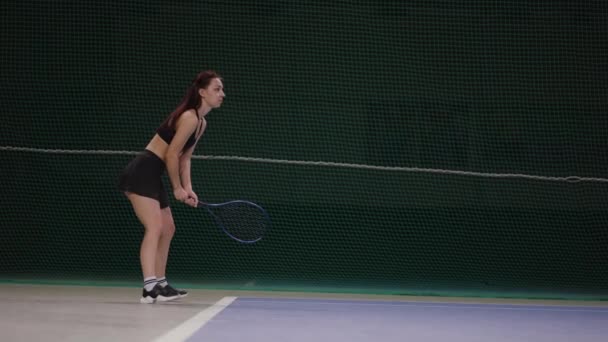 Vrouwelijke speler is het spelen van tennis op de binnenplaats, wachten dienen en slaan bal door racket, slow motion full-length schot — Stockvideo