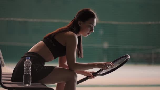 Ung sportskvinne sitter på benken på tennisbanen etter tapt kamp, trist følelse og tenkning – stockvideo