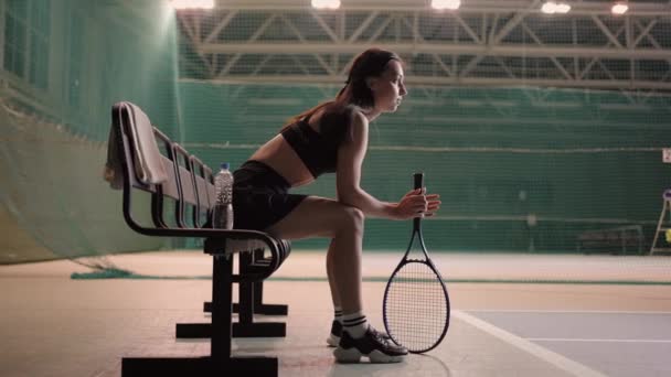 Yorgun sporcu kadın tenis kortunda oturuyor, antrenman veya maçtan sonra dinleniyor, sportif bir başlangıç yapıyor. — Stok video