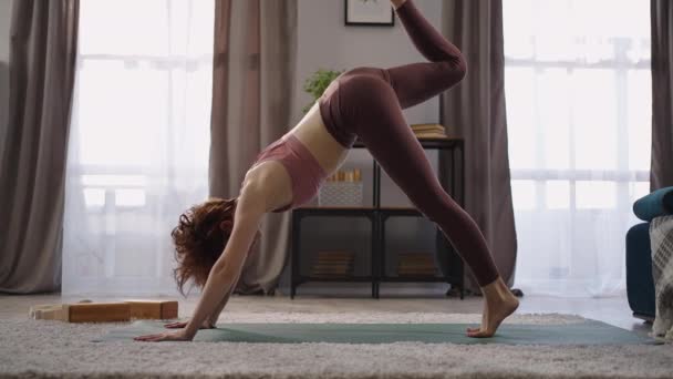 Aptitud en el hogar de la mujer entrenada, la señora deportiva está realizando asanas de yoga en la sala de estar, de pie en posición de perro orientado hacia abajo — Vídeos de Stock