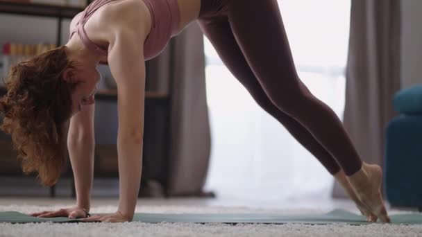 Yoga-Übungen zu Hause, erwachsene Frau trainiert im Wohnzimmer, steht in Adho Mukha Shwanasana — Stockvideo
