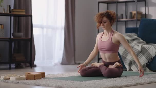 Γιόγκα εκπαίδευση της ενήλικης γυναίκας στο διαμέρισμα, κυρία κάνει σωματική άσκηση το πρωί, κάθεται στο πάτωμα — Αρχείο Βίντεο
