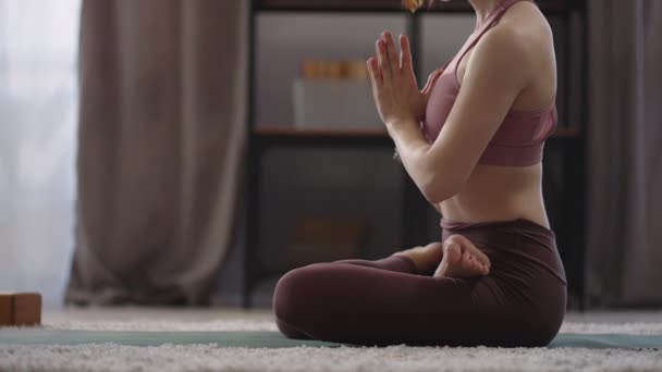 Женщина расслабляется и медитирует дома, сидя в позе лотоса в комнате, закрытые глаза, практика йоги и медитации — стоковое видео