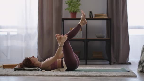 Ginástica de cura para articulações e músculos, a mulher está treinando sozinha em casa, deitada no chão, esticando a perna — Vídeo de Stock