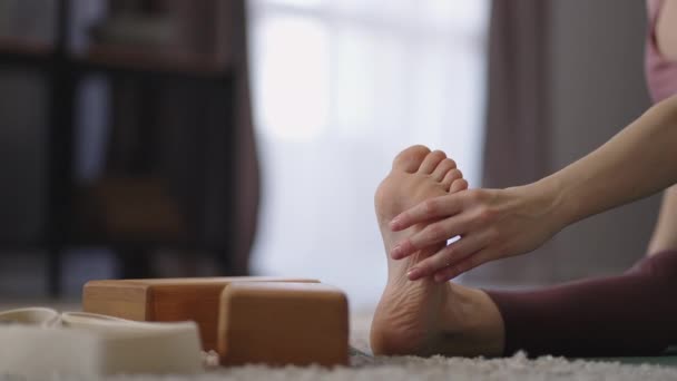Femme adulte s'entraîne seule à la maison, étirant son corps, assise sur le sol et penchant le torse à la jambe — Video