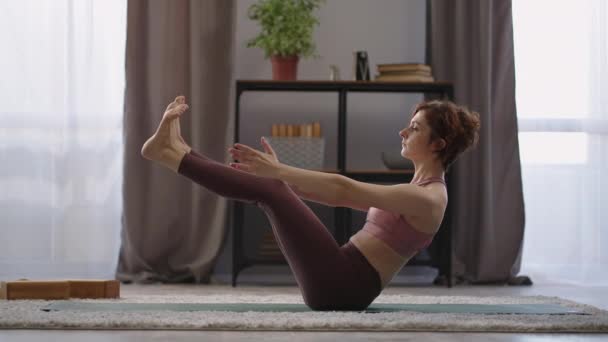 Slanke vrouw is het houden van fit, het doen van oefeningen voor slank figuur en gespierd lichaam, het uitvoeren van boot pose van yoga praktijk — Stockvideo