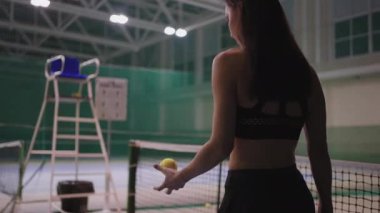 Yalnız sporcu kadın boş tenis kortunda antrenman yapıyor, genç bayan yürüyor ve topu yere atıyor.
