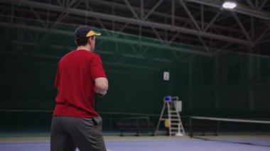 İki tenis oyuncusunun iç sahada antrenmanı, erkek ve kadın raketle topa vuruyor, yavaş çekim.