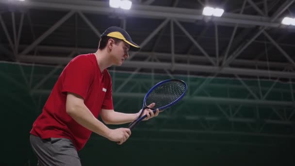 Adult tennis player is training in indoor court, medium shot of man with racquet, striking ball, slow motion — Stock Video