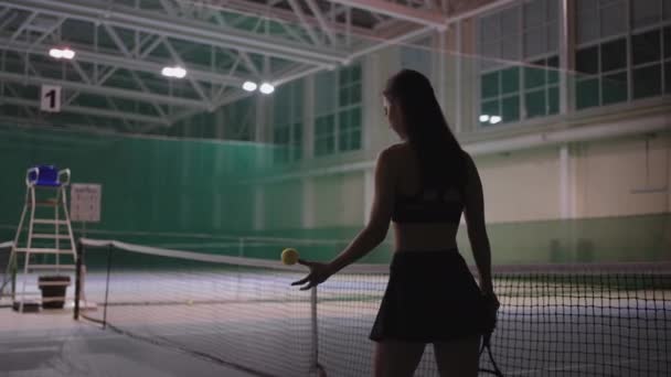 Mujer deportiva vestida ropa deportiva está caminando sobre la cancha de tenis, la celebración de raqueta de tenis y la bola de lanzamiento, vista trasera de la figura femenina delgada — Vídeos de Stock