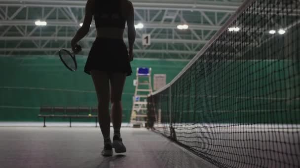 Young female tennis player is walking along net on court, back view of slender sporty figure, sport hobby — Stock Video