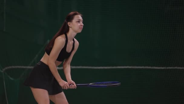 Mujer joven está entrenando en la cancha cubierta, esperando servir de oponente y golpeando la pelota por raqueta, cámara lenta — Vídeos de Stock