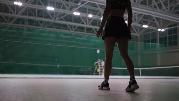 Mujer joven está entrenando en la cancha de tenis en el estadio, caminando y lanzando pelota, detalles en la parte inferior del cuerpo — Vídeos de Stock