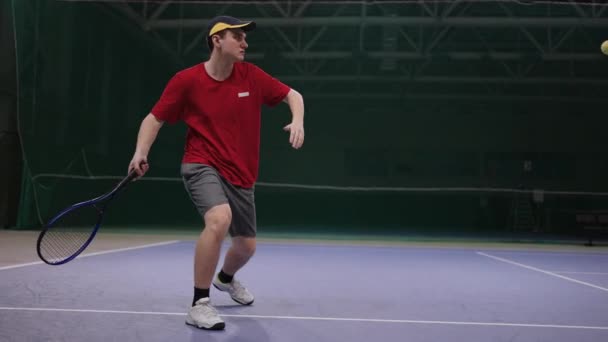 Młody mężczyzna i kobieta grają w tenisa na krytym korcie, uderzając piłkę przez rakietę, profesjonalni tenisiści trenują — Wideo stockowe