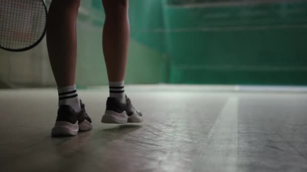 Tennista femminile sta camminando sul campo coperto, primo piano di piedi scarpe da ginnastica sportive calzate, palla da lancio, vista posteriore — Video Stock