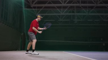 Genç yakışıklı adam stadyumun içinde tenis oynuyor, raketle topa vuruyor, yavaş çekim, orta vuruş.