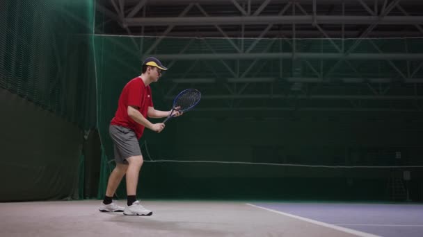 Young handsome man is playing tennis on court inside stadium, striking ball by racquet, slow motion, medium shot — Stock Video