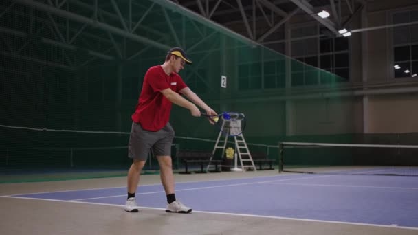 Beginning tennis player is learning to serve, full-length portrait on indoor tennis court, training and practicing strikes by racquet — Stock Video