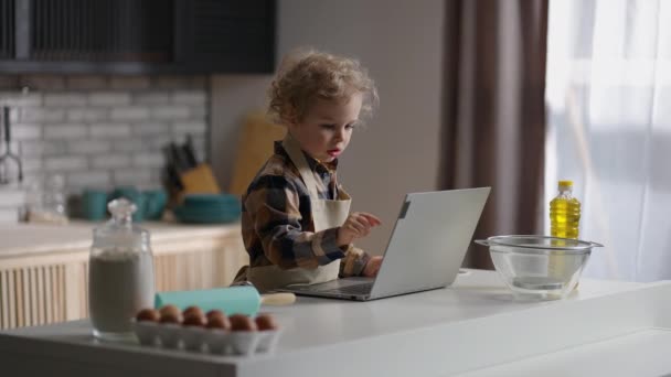 Νήπιο μαθαίνει να μαγειρεύουν, βλέποντας βίντεο για τα παιδιά στο διαδίκτυο από το laptop, παίζοντας στο σπίτι κουζίνα και μόνο — Αρχείο Βίντεο