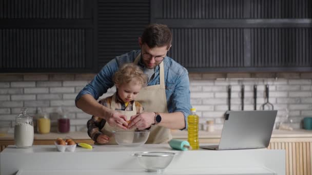 Papà sta imparando il suo bambino figlio a cucinare, giovane e bambino stanno preparando frittata per la colazione di domenica a casa cucina — Video Stock