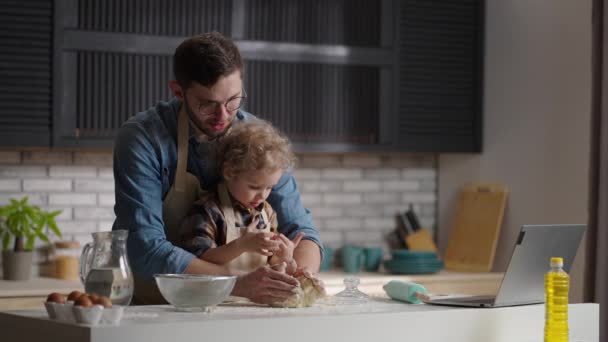 Маленький хлопчик і його батько готують хліб вдома, замішуючи тісто на столовій кухні, середній портрет — стокове відео