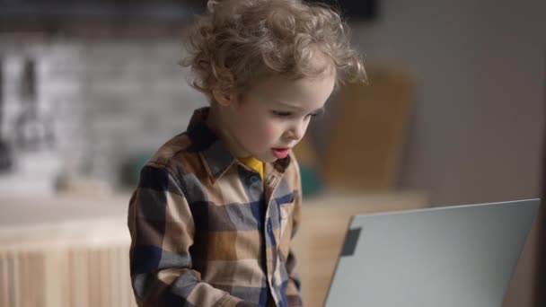 Хлопчик дошкільнята використовує сучасний ноутбук вдома, перегляд на дисплеї, натискання клавіш, середній портрет — стокове відео