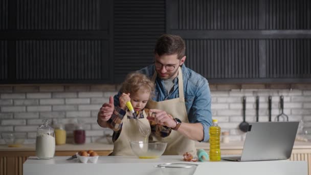 Gelukkig papa en baby zoon zijn gekleed schorten koken op huis keuken, het maken van deeg voor pannenkoeken of taart — Stockvideo