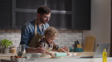 Kıvırcık saçlı küçük sevimli çocuk mutfağında hamur topluyor, babası ona yardım ediyor.