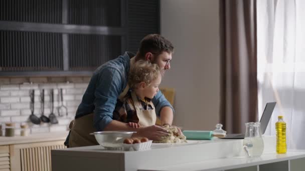 Père célibataire apprend à son petit fils à cuisiner, lecture de la recette sur Internet par ordinateur portable, cuisson de la pâte à la maison cuisine — Video