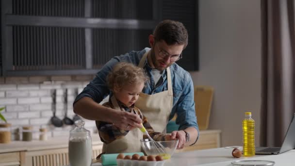 Мужчина и маленький мальчик взбивают яйца для омлета, отец учится готовить на домашней кухне, проводить время вместе — стоковое видео