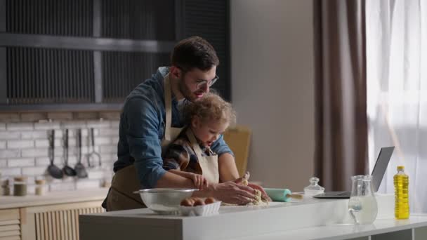 Vader en peuter zoon koken via internet recept, op zoek naar laptop en het maken van deeg op keukentafel, vader en baby jongen — Stockvideo