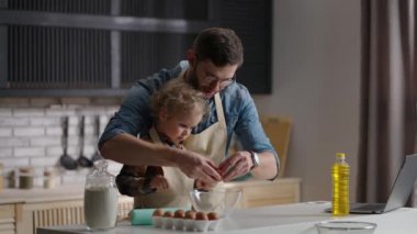 Baba küçük oğluna mutfakta omlet pişirmeyi öğretiyor. Adam kasede yumurta kırıyor.