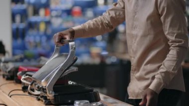 Erkek alışverişçi ev aletleri mağazasında iki elektrikli ızgarayı karşılaştırıyor. El ve numunelerin yakın görüntüsü.