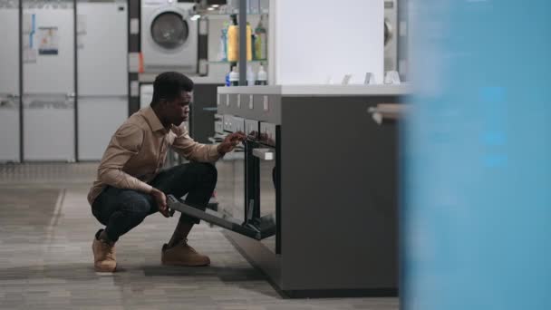 Negro chico está de compras en la tienda de electrodomésticos, la elección de equipos para la cocina del hogar, estufa de visualización — Vídeos de Stock