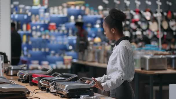 Jonge afro-Amerikaanse vrouw is winkelen in huis apparaat winkel in winkelcentrum, kiezen voor elektrische grill — Stockvideo