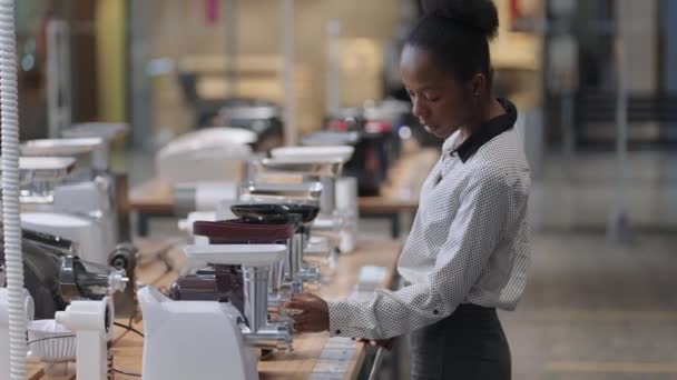 Comprar moedor de carne elétrica na loja de eletrodomésticos, mulher negra está vendo amostras na área de comércio — Vídeo de Stock