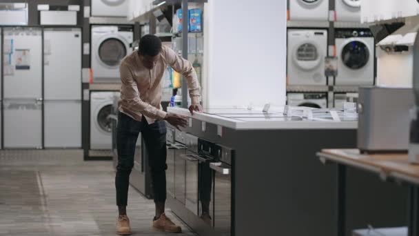 Νεαρός Αφρο-Αμερικανός βλέπει κουζίνες σε κατάστημα υλικού, επιλέγοντας κουζίνα για οικιακή χρήση — Αρχείο Βίντεο