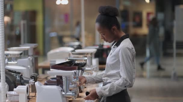 Jeune dame noire choisit broyeur de viande électrique dans la quincaillerie, visualisation de l'échantillon d'exposition sur l'étagère dans la zone commerciale — Video