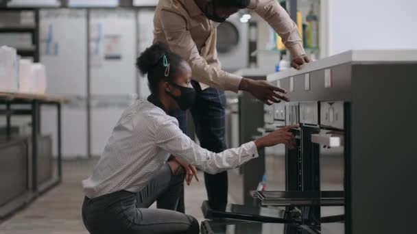 Jong zwart getrouwd stel kiezen oven in huishoudapparaat winkel in winkelcentrum, mensen met gezichtsmaskers van coronavirus — Stockvideo