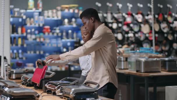 Young afro-american married couple is choosing electric waffle iron or grill in home appliances store — Stock Video